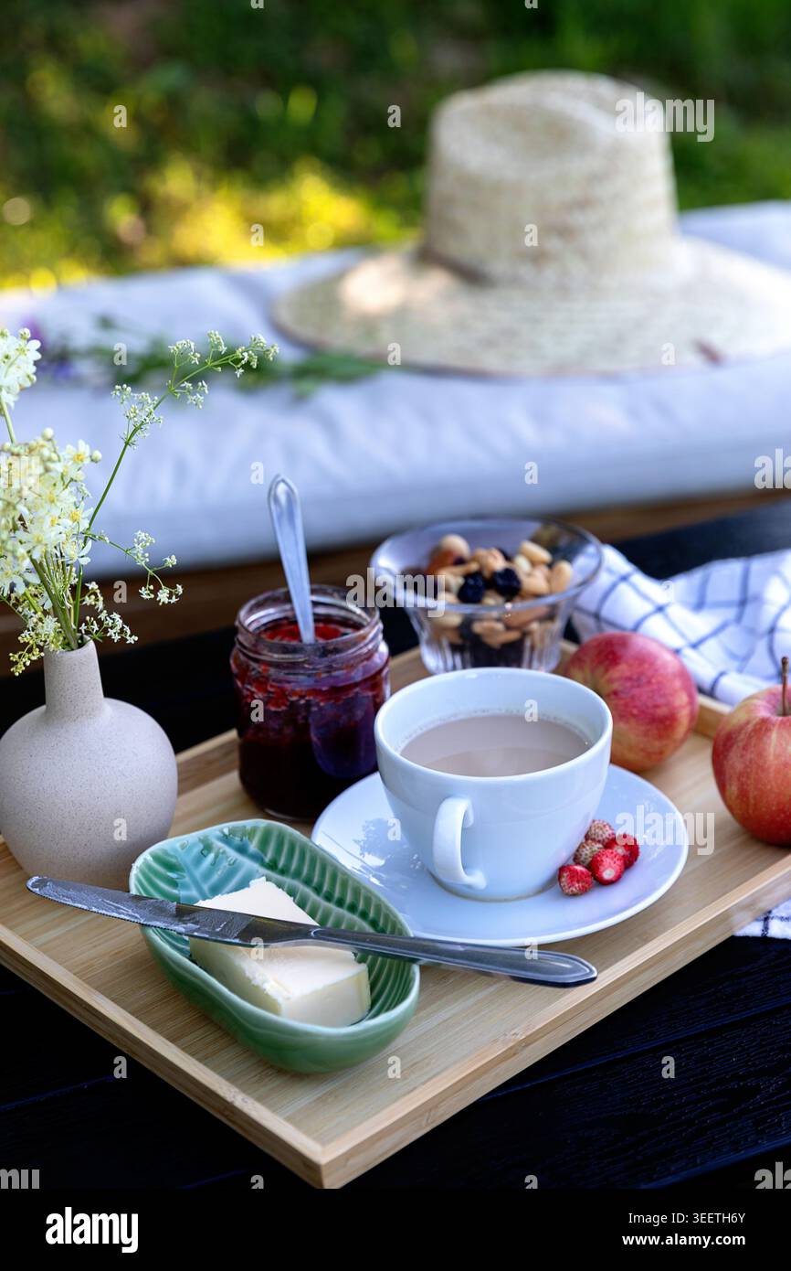 Una deliziosa colazione fatta in casa servita su un vassoio di legno rustico con caffè fresco, marmellata, burro e un bellissimo vaso di fiori di campo. Foto Stock