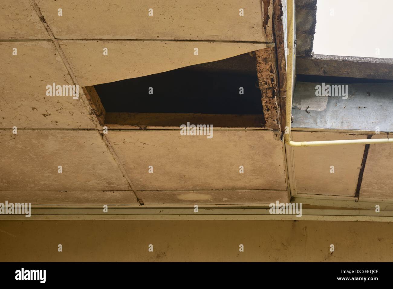 buco nel vecchio soffitto bianco sporco delle piastrelle acustiche, tetto esterno danneggiato, concetto di danno alla proprietà Foto Stock