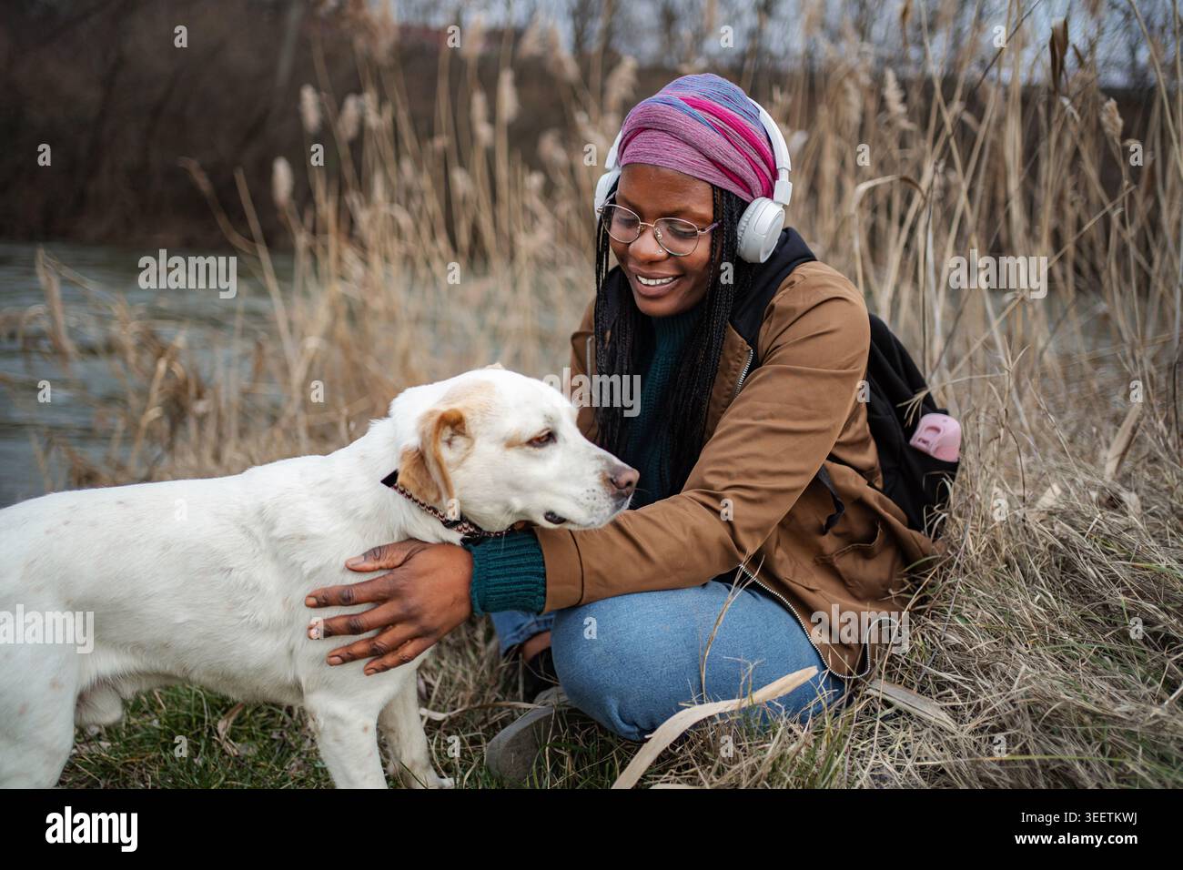 Felice giovane donna adulta che accarezza il cane in natura ascoltando musica Foto Stock