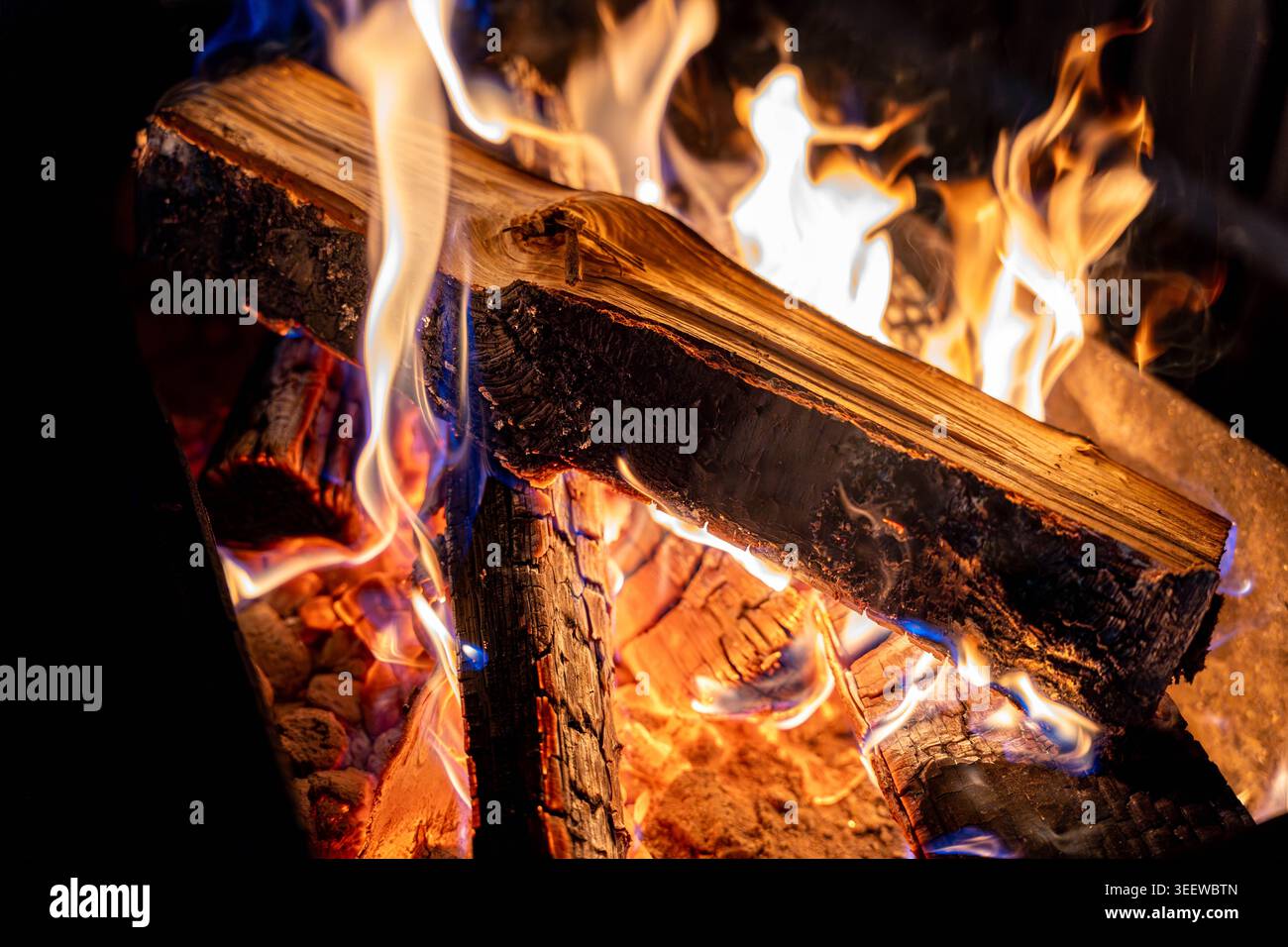 Fuoco di tronco incandescente con fiamme danzanti ed Embers, primo piano di tronchi di legno duro ardente, linguette di fiamma blu e arancione, carbone ardente, rustico caldo Foto Stock