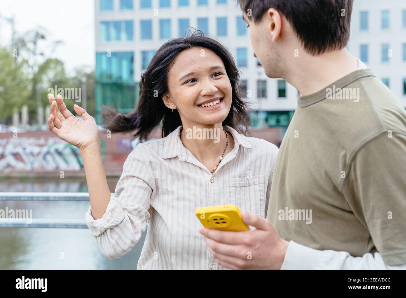 Elegante donna asiatica con smartphone giallo che registra vlog o feed a scorrimento in un'area urbana moderna Foto Stock