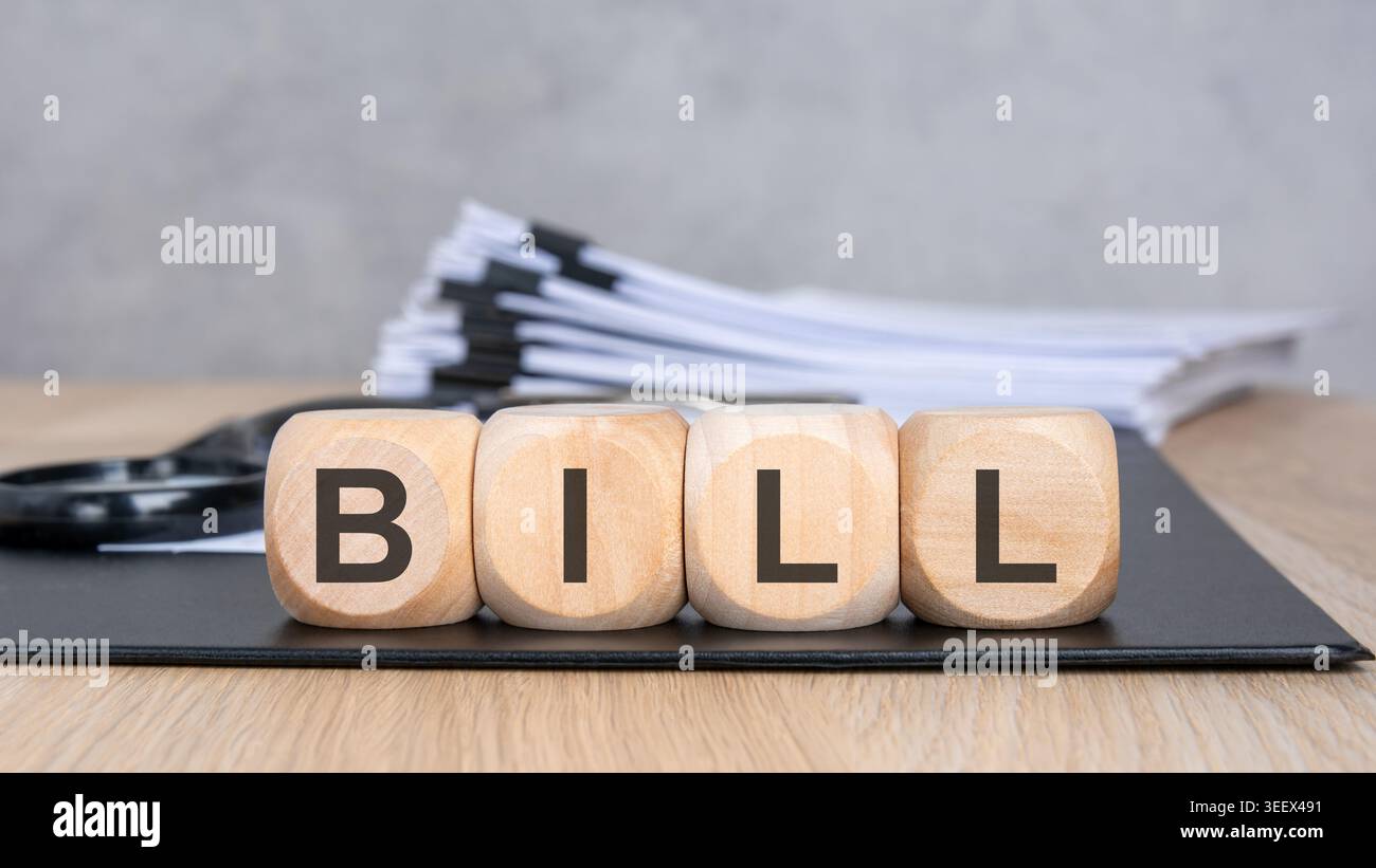 Cubi di legno con la parola BILL su un portadocumenti nero. Una pila sfocata di documenti aziendali e una lente di ingrandimento sullo sfondo. Concetto di Invoic Foto Stock