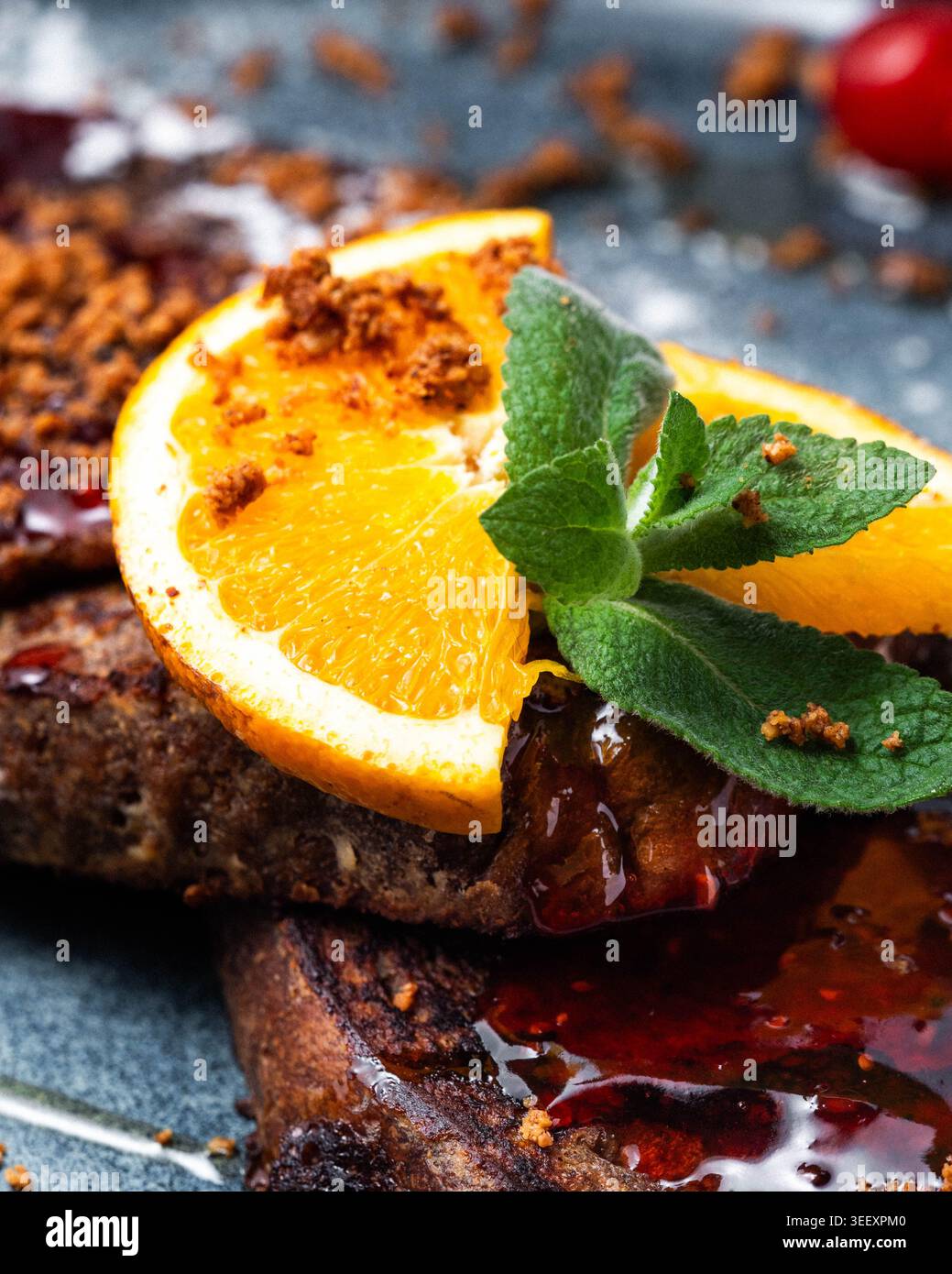 Pancake scuri ricchi e conditi con sciroppo. Fetta di arancia e foglie di menta guarnire la parte superiore. Le briciole di zucchero di canna cospargono la superficie. La vivace bacca rossa aggiunge un Foto Stock