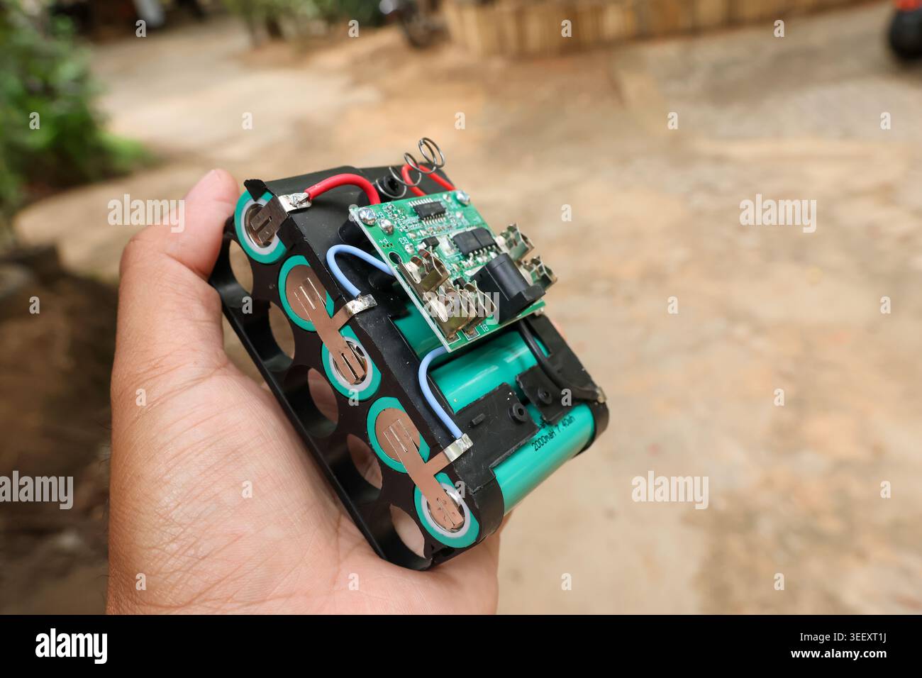 Persona che tiene la mano la batteria al litio personalizzata con il componente elettronico del modulo scheda a circuito stampato verde montaggio attento del progetto fai da te che esprime la Foto Stock