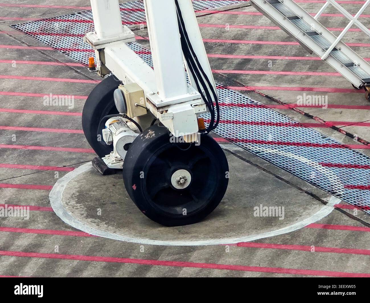 Dettaglio ravvicinato delle ruote industriali per impieghi gravosi base della struttura della piattaforma in metallo in piedi saldamente superficie del pavimento in calcestruzzo con linee di avvertimento rosse che riflettono Foto Stock
