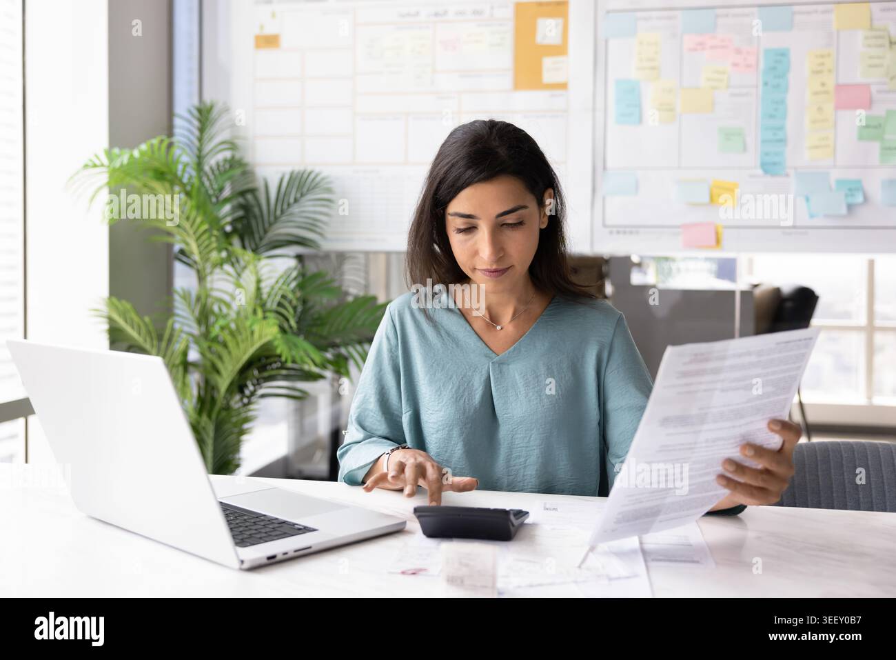Donna professionale concentrata che prepara report o riepilogo del budget sul posto di lavoro Foto Stock