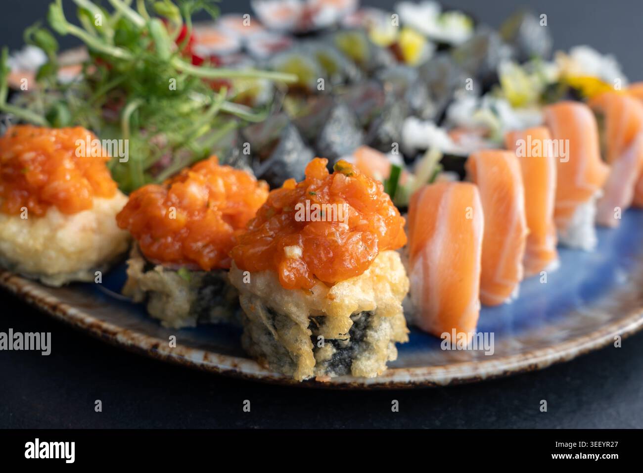 Sushi tempura croccanti ricoperti di salmone piccante, microgreen freschi, dolci assortiti di maki e fiori commestibili su un set di piatti di sushi Foto Stock