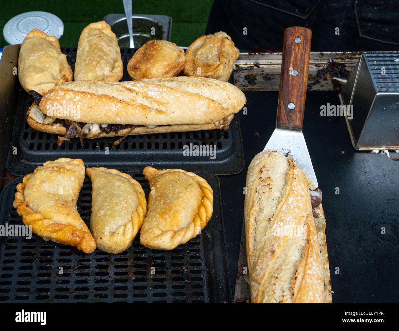Empanadas su un grill, deviatoi e baguette. Panini croccanti, cibo di strada con vari ripieni, piatti pronti da mangiare durante il festival gastronomico, cucina Foto Stock