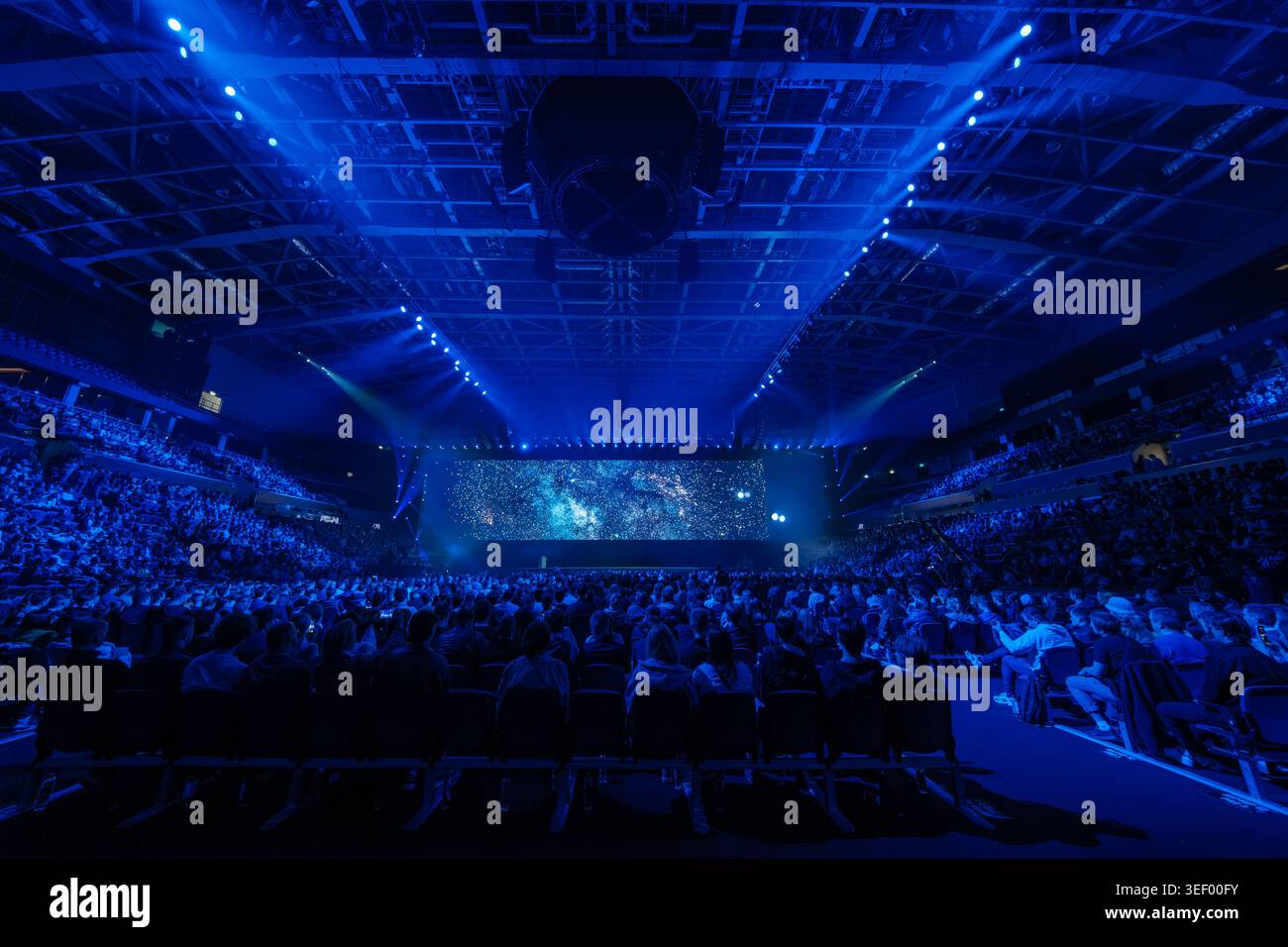 Il pubblico dell'arena è pieno di spettatori che guardano il palco blu illuminato con proiezioni stellate, luci coinvolgenti e un'atmosfera da eventi dal vivo. Foto Stock