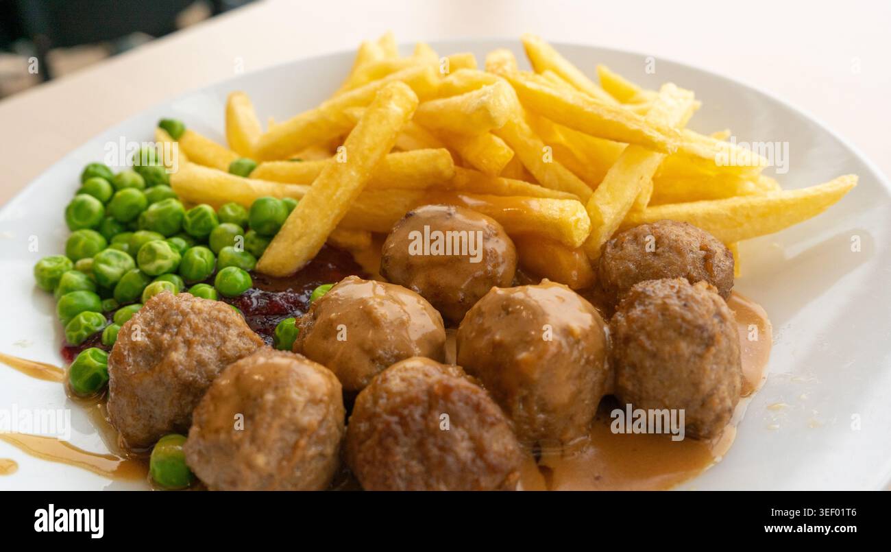 Polpette con patatine fritte, piselli verdi, salsa di besciamella e marmellata di mirtilli, polpette di carne su piatto bianco primo piano tipico del cibo svedese, vitoulet belga me Foto Stock