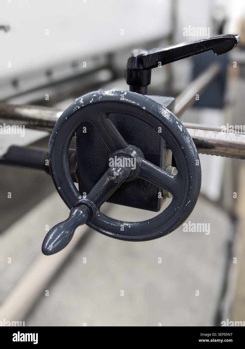 Volantino valvola nero con manico a leva posizionato sul gruppo tubi, superficie in fusione testurizzata, teste di bulloni visibili e sfondo industriale suggerimento segue Foto Stock
