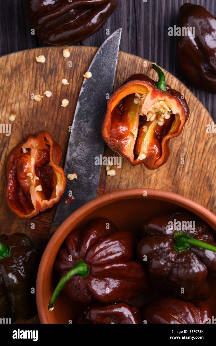 Peperoni habanero al cioccolato con coltello e ciotola su una superficie di legno. Preparazione di cialde di peperoncino fresco per lo styling naturale degli alimenti Foto Stock
