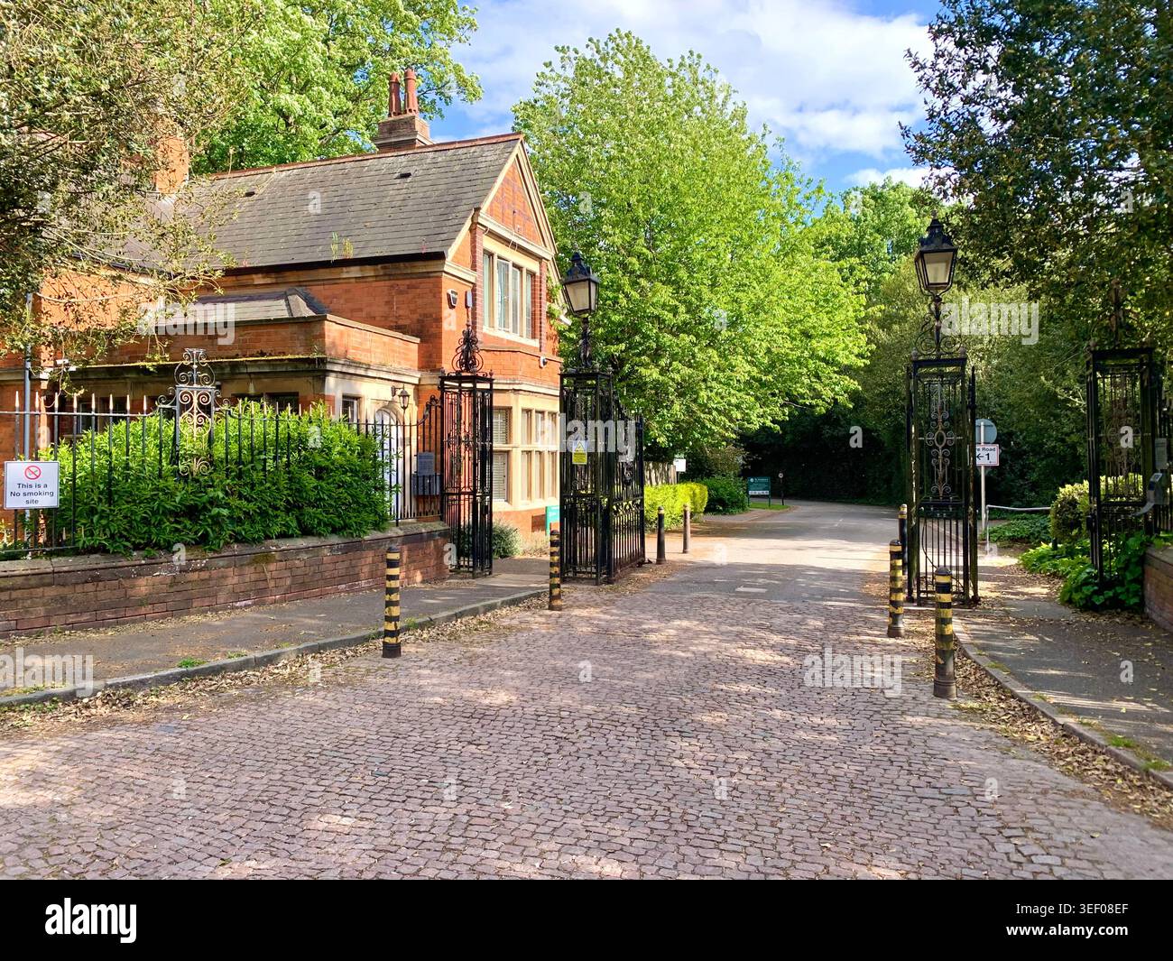 Storici cancelli d'ingresso e Lodge in mattoni rossi al St Andrews Hospital di Northampton, Inghilterra, un tranquillo approccio alberato a uno dei più antichi manicomi del Regno Unito - Immagine stock catturata con smartphone