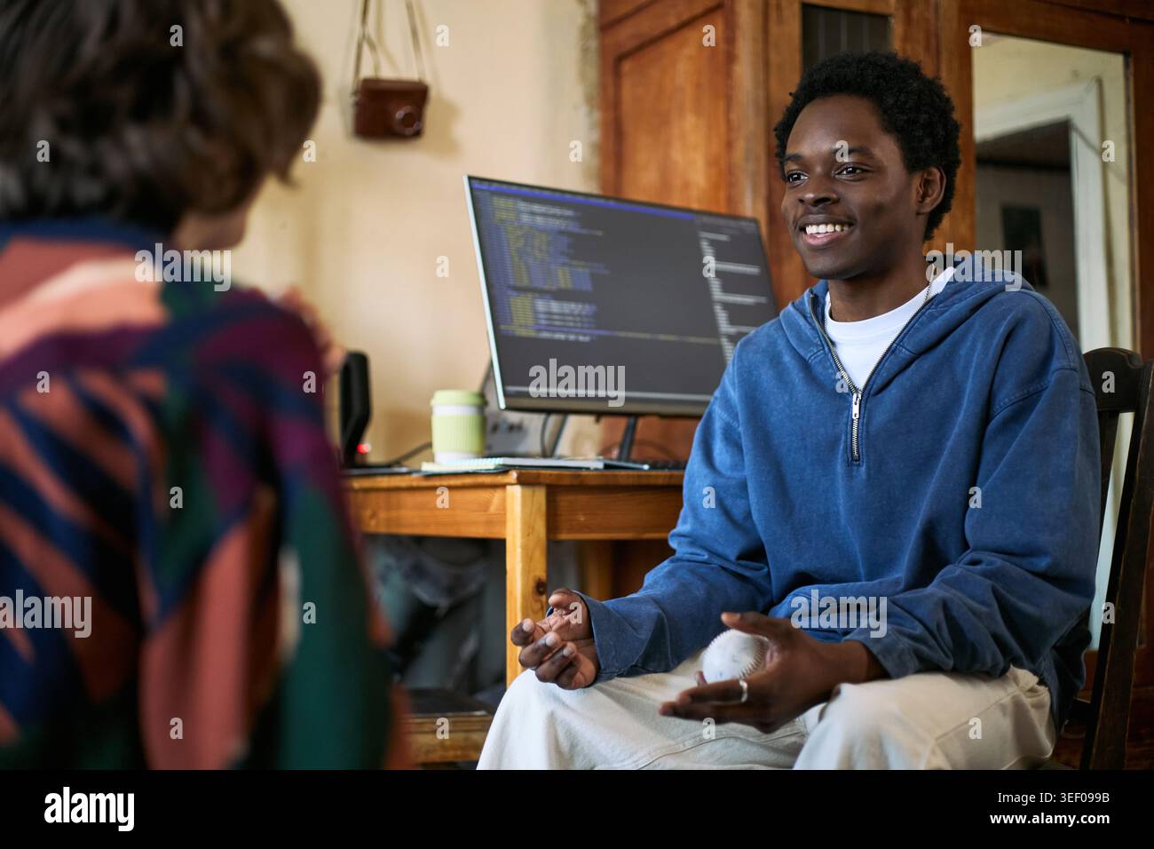 Giovane uomo di colore che parla dello sviluppo software con un'amica accanto al monitor di codifica, che rappresenta il lavoro di squadra e il mentoring tecnico. Programmazione dell'istruzione, assunzione di startup, collaborazione remota Foto Stock