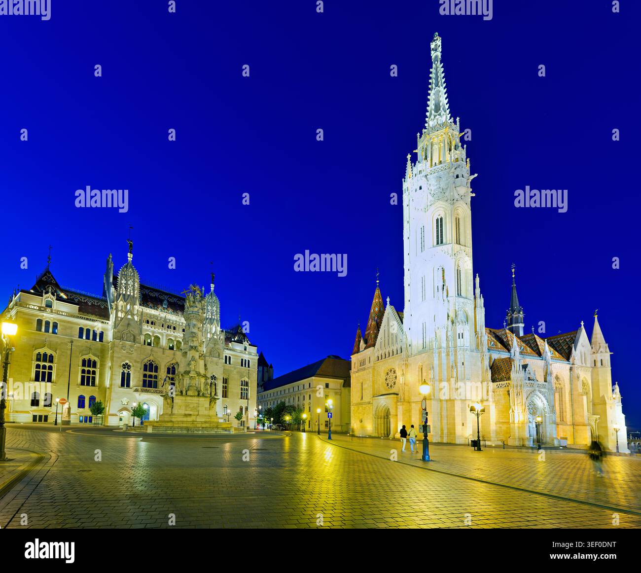 La chiesa di Mattia e il Ministero dell'interno si trovano sotto il cielo del tramonto a Budapest. Le persone camminano nelle vicinanze, godendosi la vista e la luce della sera. Foto Stock