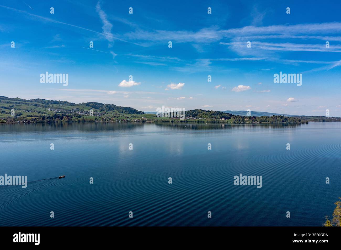 Vista panoramica sul litorale del lago Zug e sulle colline ondulate - acque blu tranquille con piccola barca e increspature Foto Stock