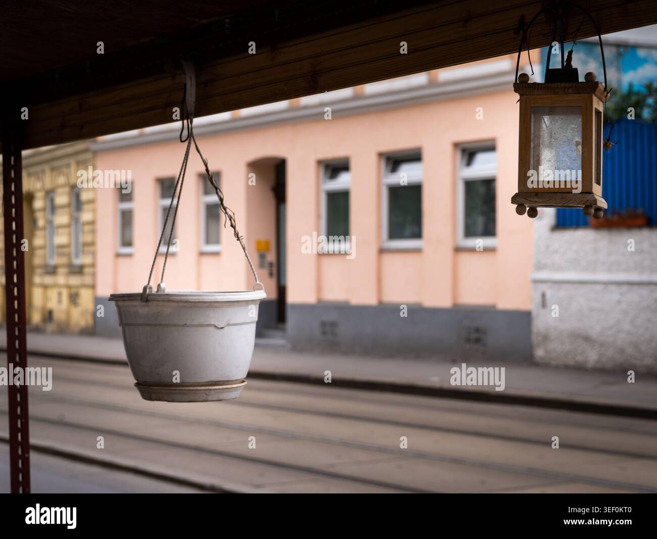 Vienna, Austria - 16 aprile 2021: Vaso di fioriera di plastica bianca e piccola lanterna di legno pendono dalla trave di riparo della fermata del tram ondulato accanto al tram d'acciaio tra Foto Stock