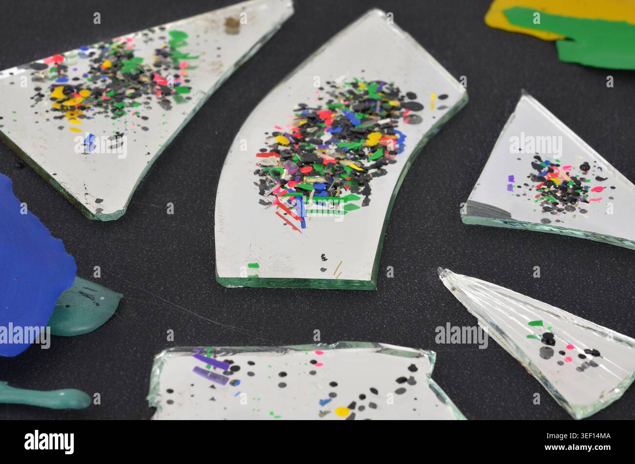 Piccoli pezzi di plastica colorati riflessi in uno specchio rotto su sfondo scuro. Bassa profondità di campo - spazzatura come astrazione. Foto Stock