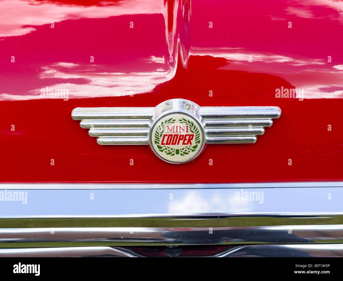 Primo piano di uno stemma rosso vintage Mini Cooper con ali cromate su un cofano rosso brillante Foto Stock