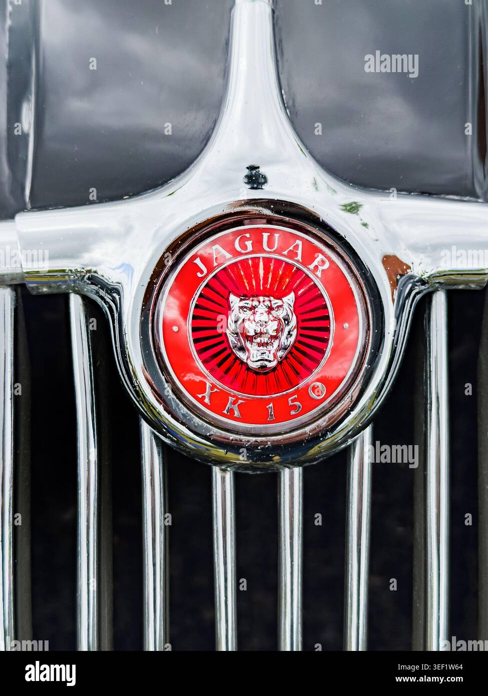 Primo piano di un emblema rosso Jaguar XK 150 montato su una griglia del radiatore cromata di una classica auto sportiva britannica Foto Stock