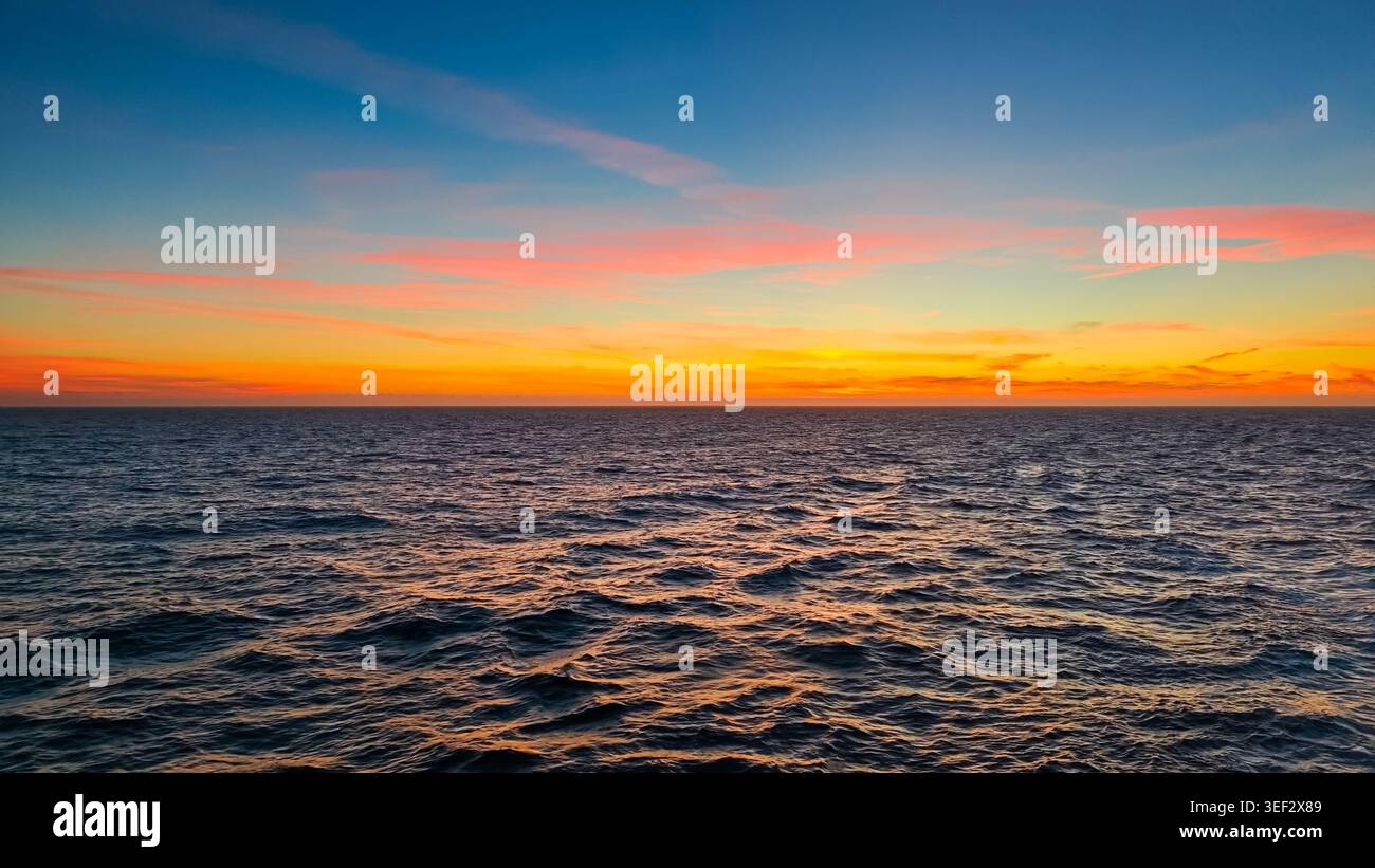 Oceano Pacifico, Oceano Pacifico - 17 agosto 2024: Il tramonto dorato si illumina sulla superficie ondulata dell'Oceano Pacifico, Alaska. Le nuvole sono colorate di rosa e di arancia Foto Stock