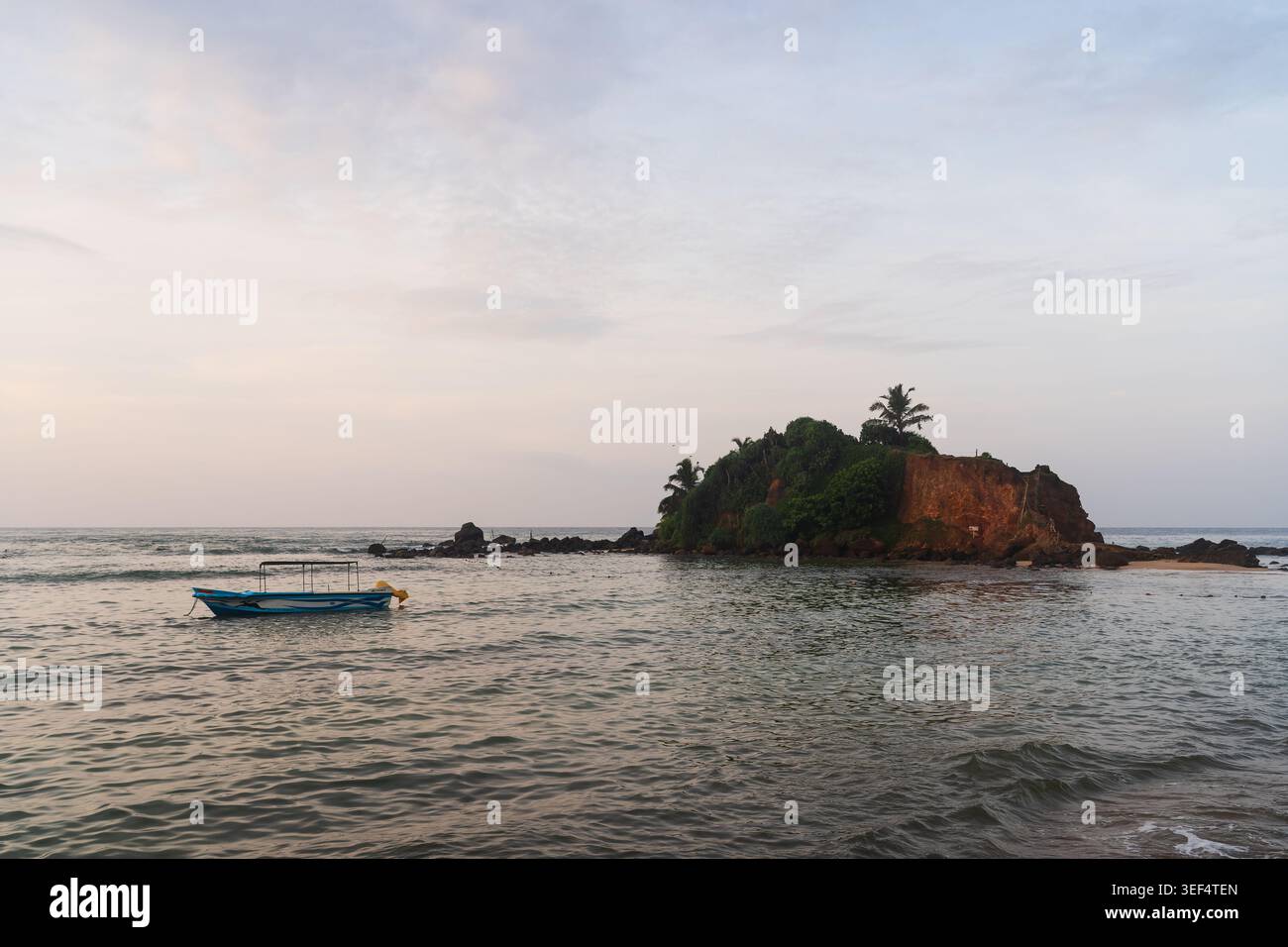 Un piccolo motoscafo turistico che galleggia sulle calme acque marine vicino all'isola Parrot Rock a Mirissa, Sri Lanka, al crepuscolo. Foto Stock