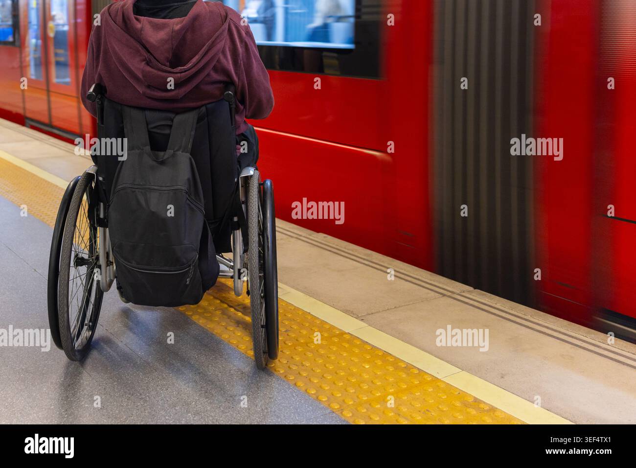 La persona con disabilità siede su una sedia a rotelle in una stazione ferroviaria mentre attende l'arrivo del treno accessibile. Foto Stock