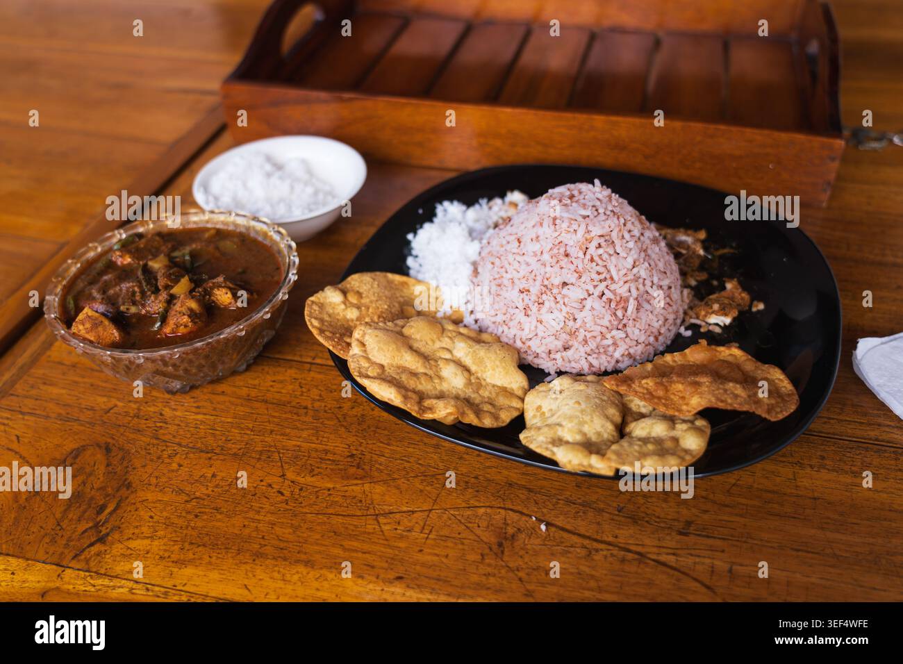 Tradizionale riso e curry dello Sri Lanka servito su un tavolo di legno con riso rosso, pol sambol, papadam e salsa piccante al curry Foto Stock