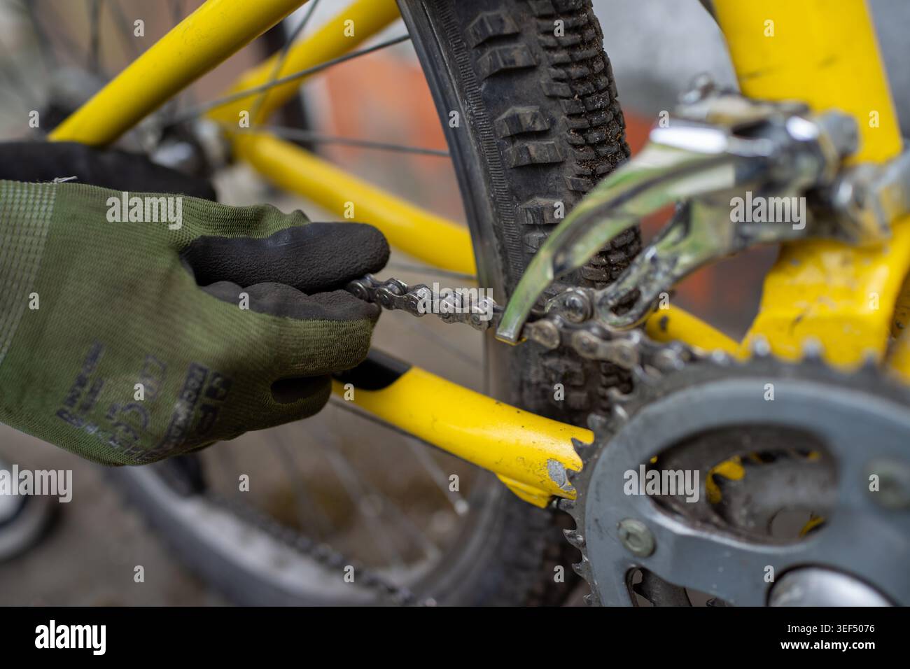 Primo piano volontario che regola il deragliatore e la catena su una bicicletta gialla, indossando i guanti con le pinze per allineare gli ingranaggi, Foto Stock