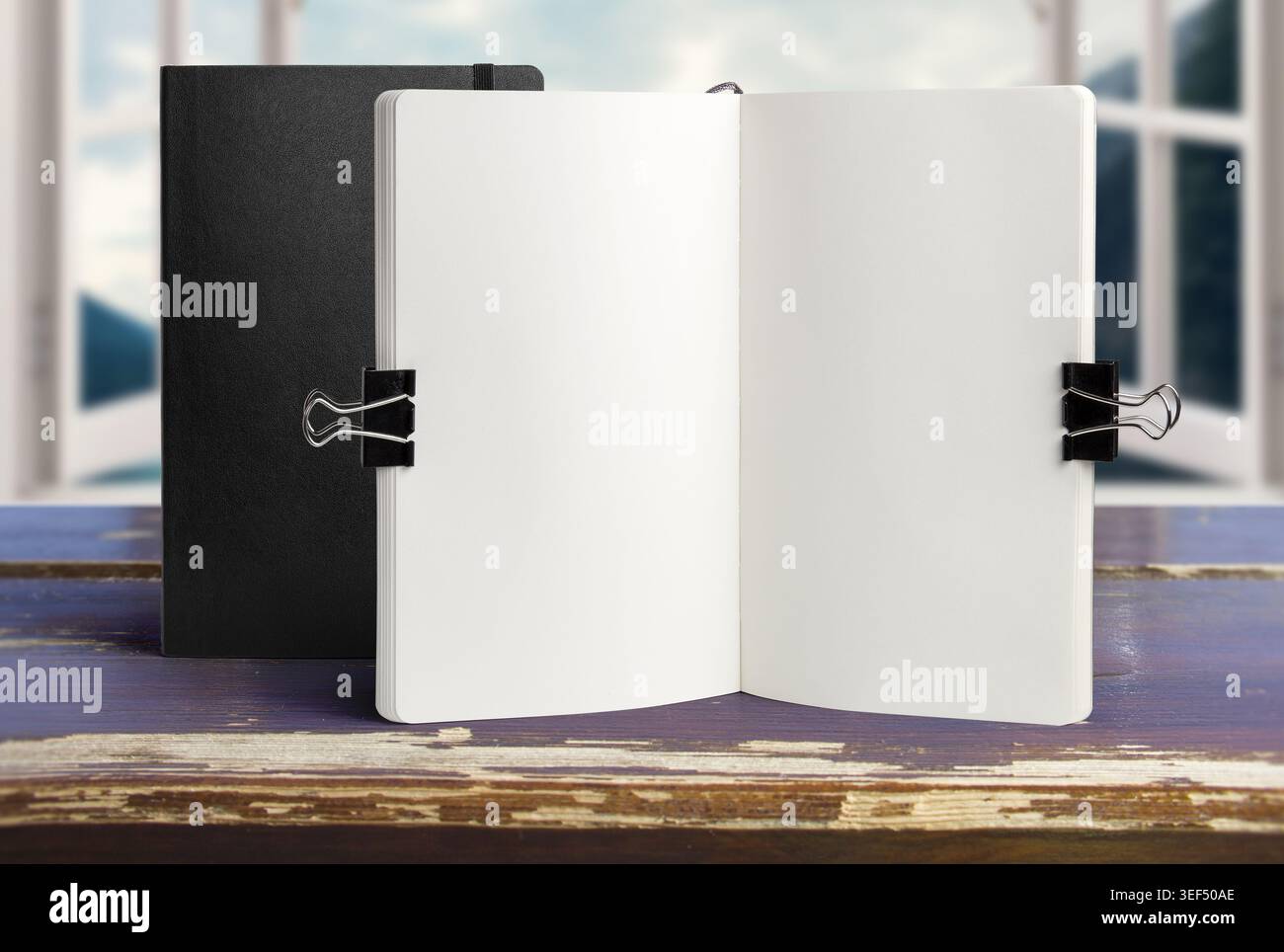 Apri il modello bianco del notebook su un tavolo in legno con clip per ufficio e piante decorative. Schema di schizzo o modello di menu in un'area di lavoro luminosa Foto Stock