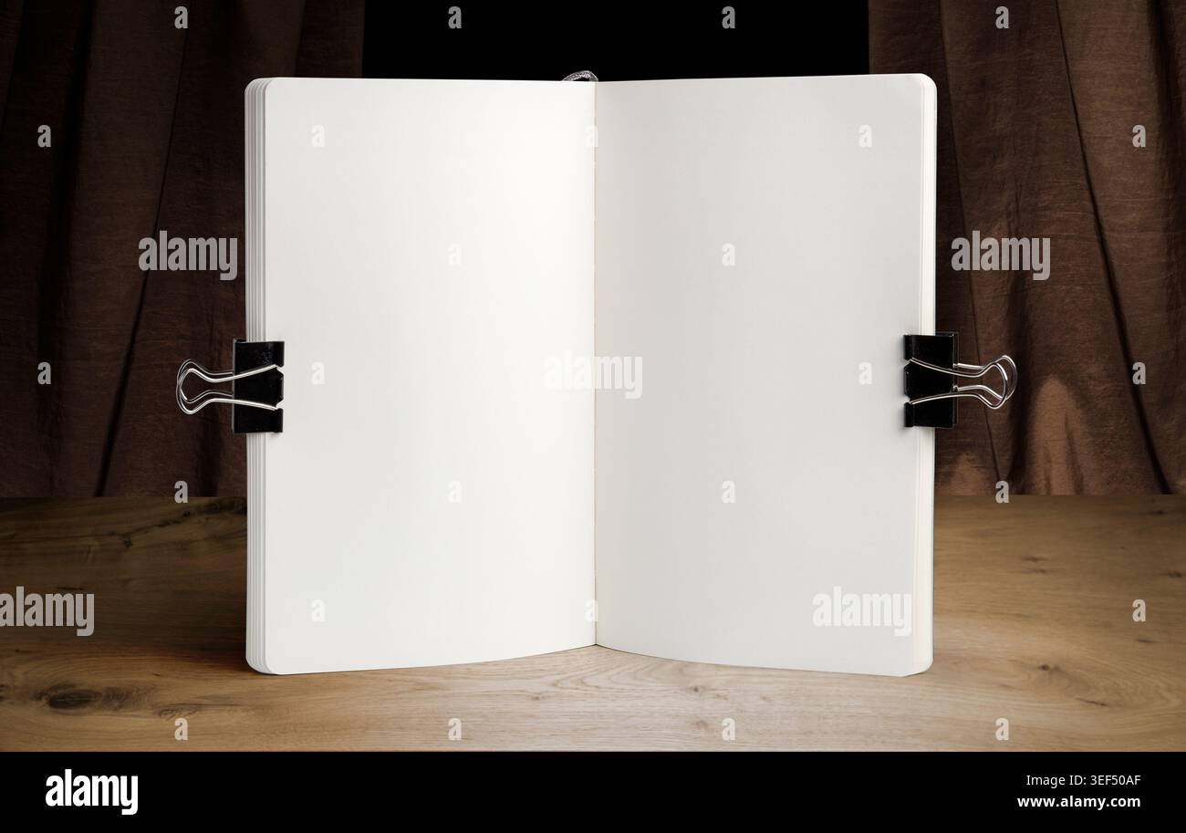 Apri il modello bianco del notebook su un tavolo in legno con clip per ufficio e piante decorative. Schema di schizzo o modello di menu in un'area di lavoro luminosa Foto Stock