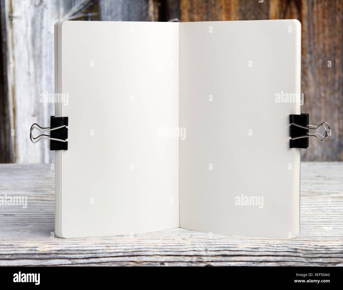 Apri il modello bianco del notebook su un tavolo in legno con clip per ufficio e piante decorative. Schema di schizzo o modello di menu in un'area di lavoro luminosa Foto Stock