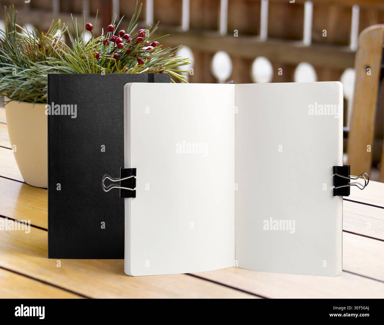 Apri il modello bianco del notebook su un tavolo in legno con clip per ufficio e piante decorative. Schema di schizzo o modello di menu in un'area di lavoro luminosa Foto Stock
