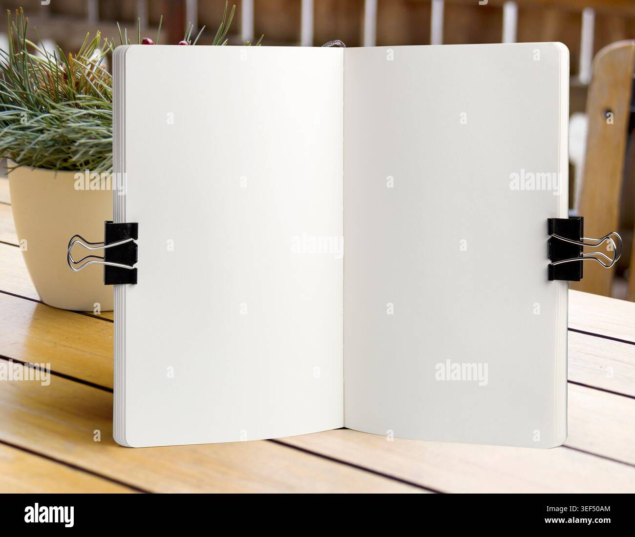 Apri il modello bianco del notebook su un tavolo in legno con clip per ufficio e piante decorative. Schema di schizzo o modello di menu in un'area di lavoro luminosa Foto Stock