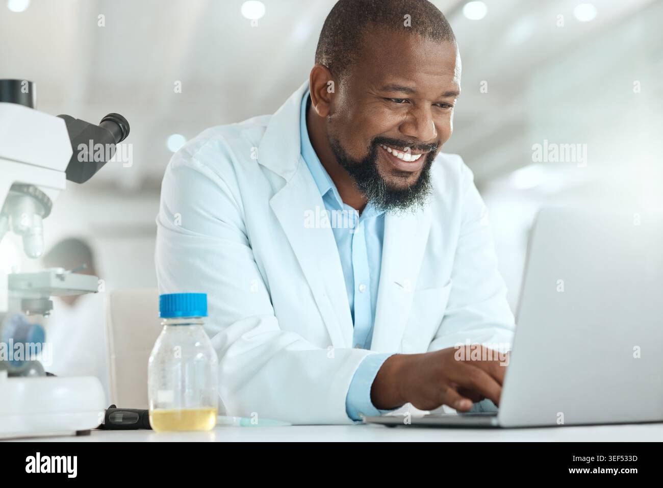 Laboratorio, computer portatile e medico sorridente per la ricerca, la soluzione e il test per l'analisi del dna. Digitazione, tecnologia e uomo nero con conoscenze specialistiche Foto Stock