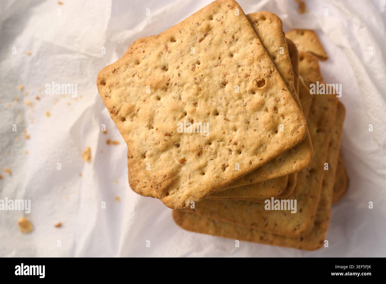 pila di cracker quadrati di grano integrale su carta bianca, consistenza croccante del biscotto, vista dall'alto con messa a fuoco morbida, snack salutari e cucina Foto Stock