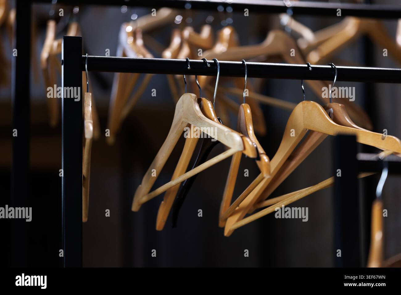 Fila di grucce in legno marrone vuote su un rack in una stanza poco illuminata con ombre profonde. Concetto di crisi economica al dettaglio, chiusura di negozi di moda, minimali Foto Stock
