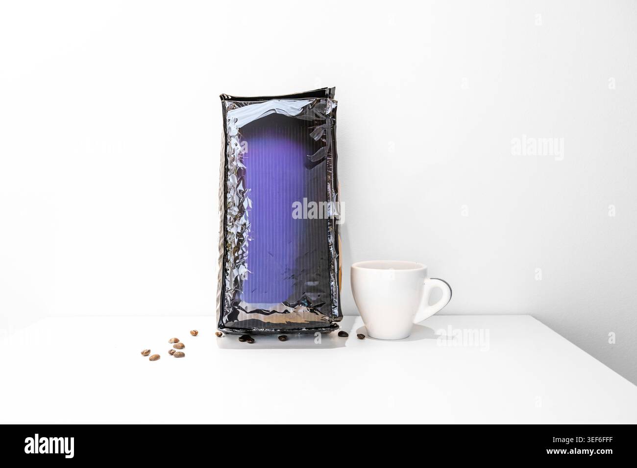Una scatola ermetica blu scuro con chicchi di caffè e una tazza su una superficie bianca. Foto Stock
