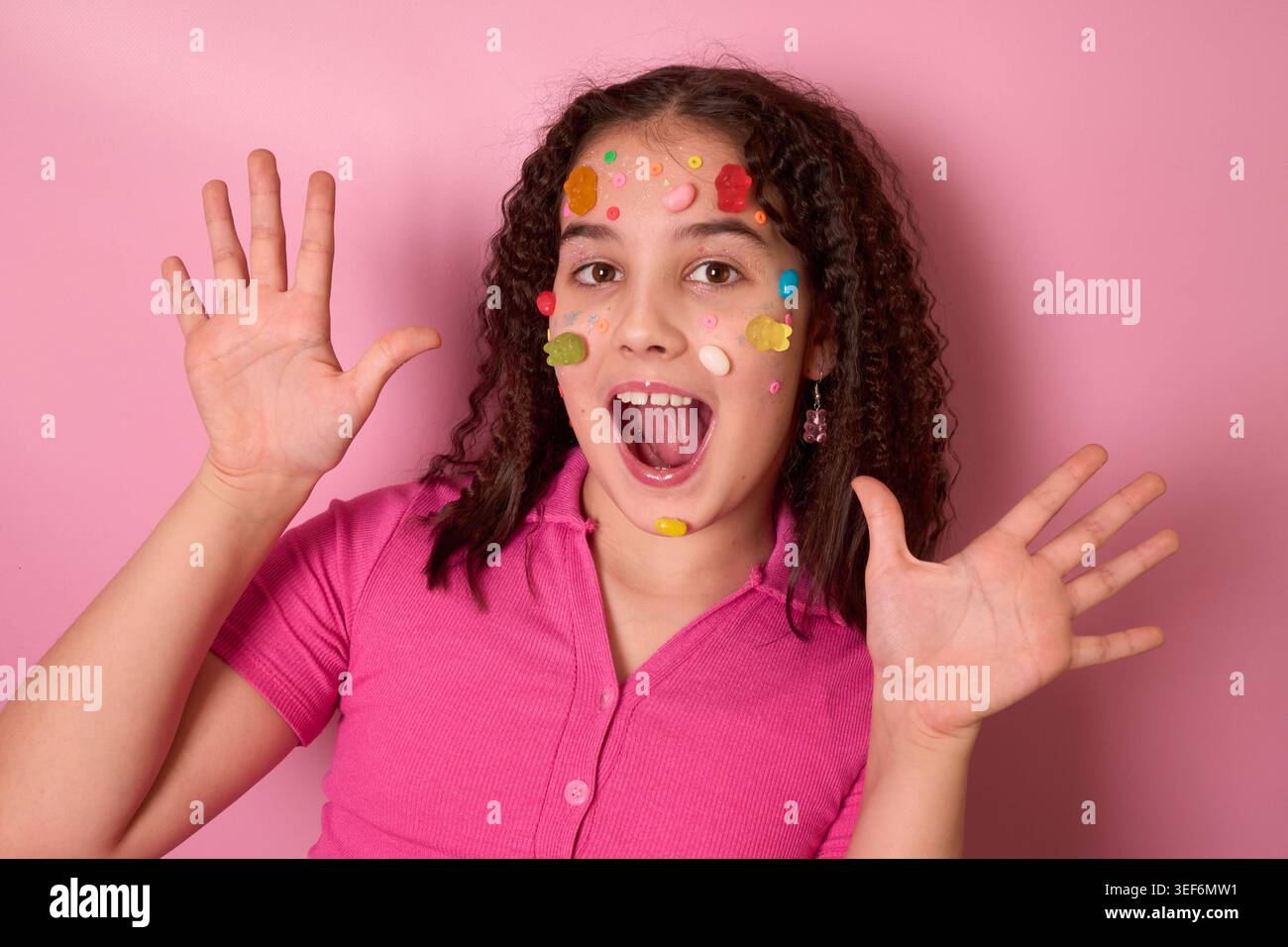 Playful Girl con caramelle colorate ed espressioni su uno sfondo rosa brillante in Joyful Art Foto Stock