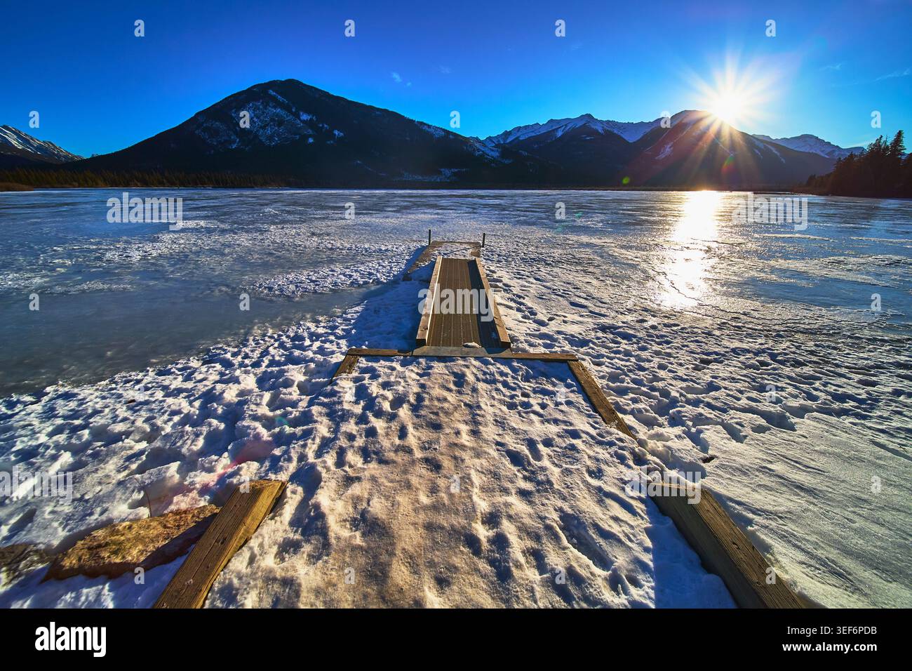 Molo invernale sul lago ghiacciato con Sunburst e Mountain a Snowy Wilderness Foto Stock