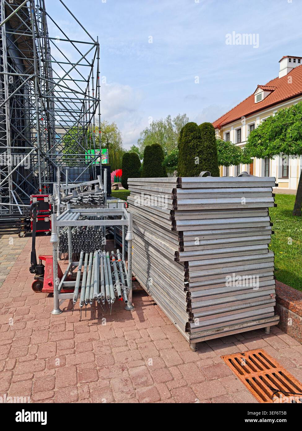Allestimento di palcoscenici all'aperto con piattaforme in alluminio impilate, ponteggi e attrezzature per il rigging vicino a un parco e a un edificio residenziale. Foto Stock