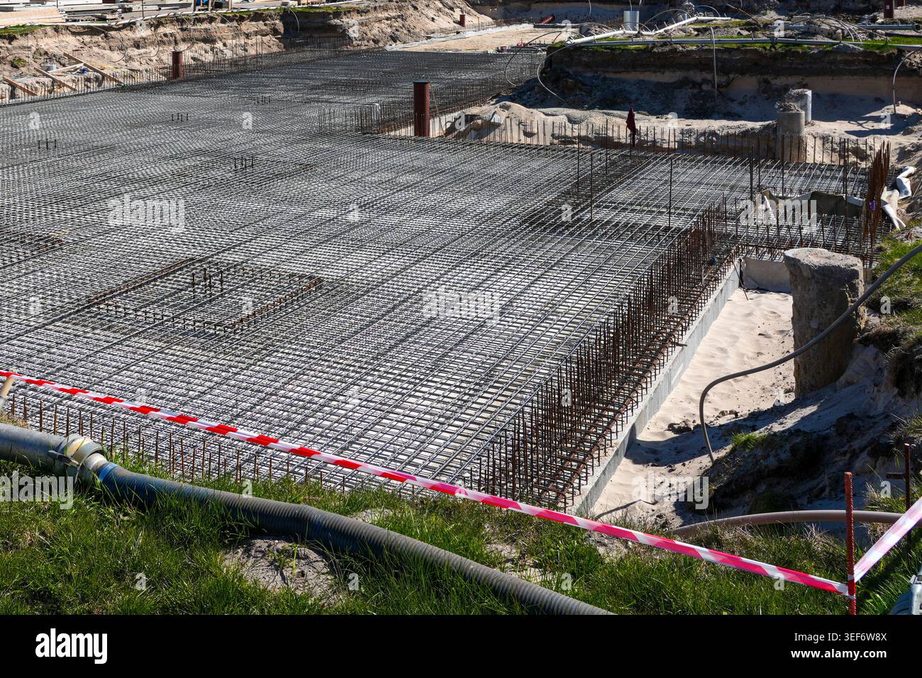 Ampia visuale delle fondamenta a rete in acciaio rinforzato con griglia per tondini e cassaforma, pronte per il versamento di calcestruzzo in un cantiere di grandi dimensioni Foto Stock