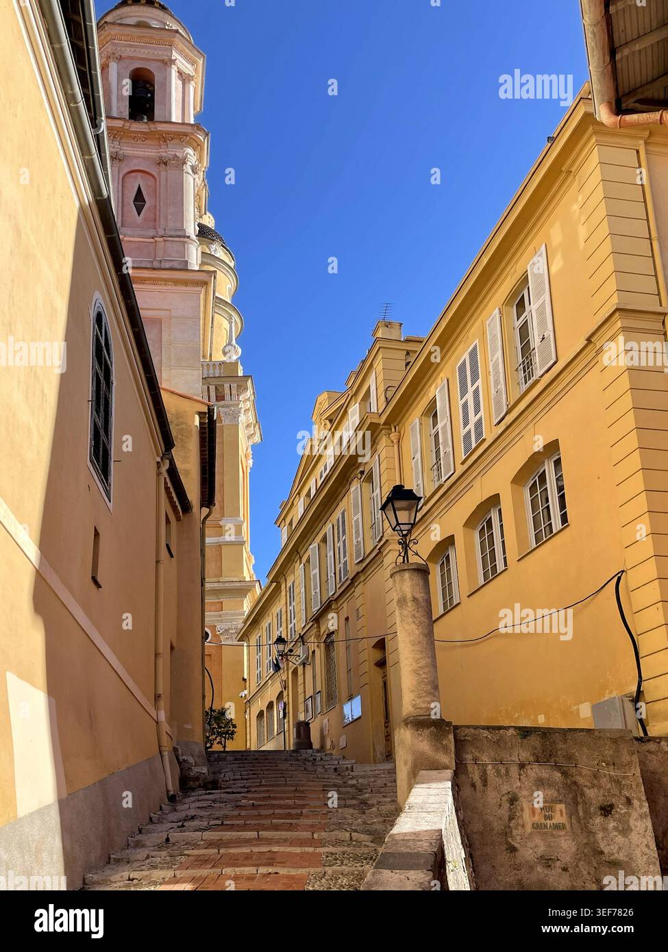 Mentone, Francia. Scala nella città vecchia, con vista sulle torri della Chapelle des Pénitents-Blancs e della basilica Saint-Michel Archange de Menton. - Immagine stock catturata con smartphone