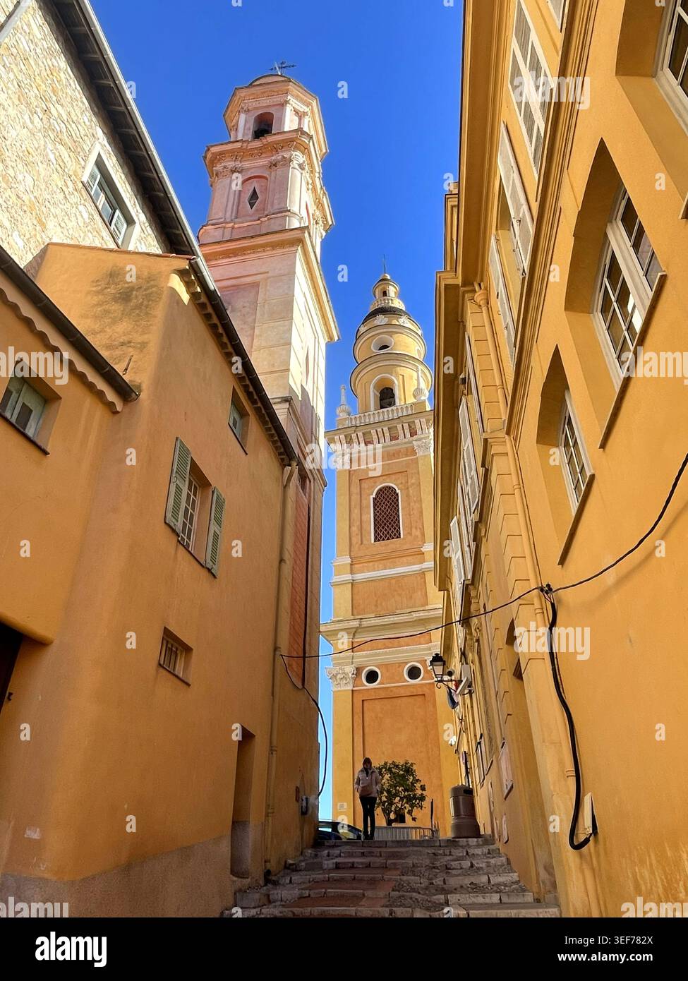 Mentone, Francia. Scala nella città vecchia, con vista sulle torri della Chapelle des Pénitents-Blancs e della basilica Saint-Michel Archange de Menton. - Immagine stock catturata con smartphone