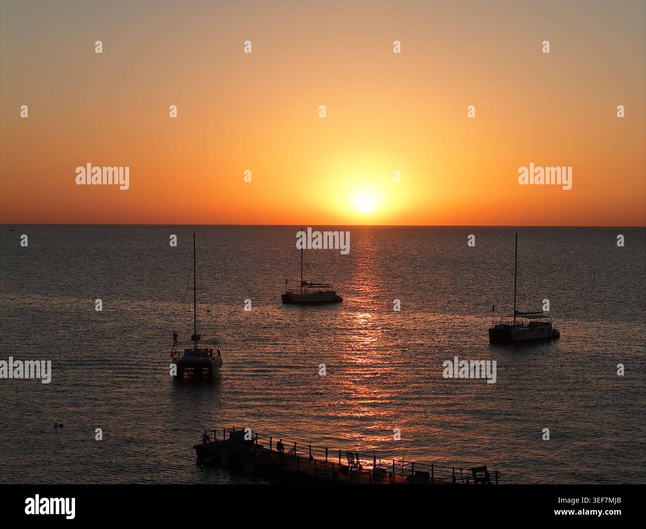 Tramonto sul mare calmo con barche a vela e molo Foto Stock