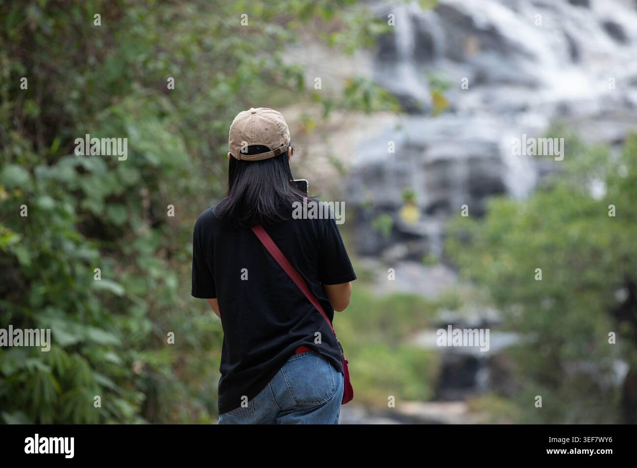 Turista donna che scatta foto della cascata con smartphone, comportamento di utilizzo dello smartphone durante il viaggio, vista posteriore Foto Stock