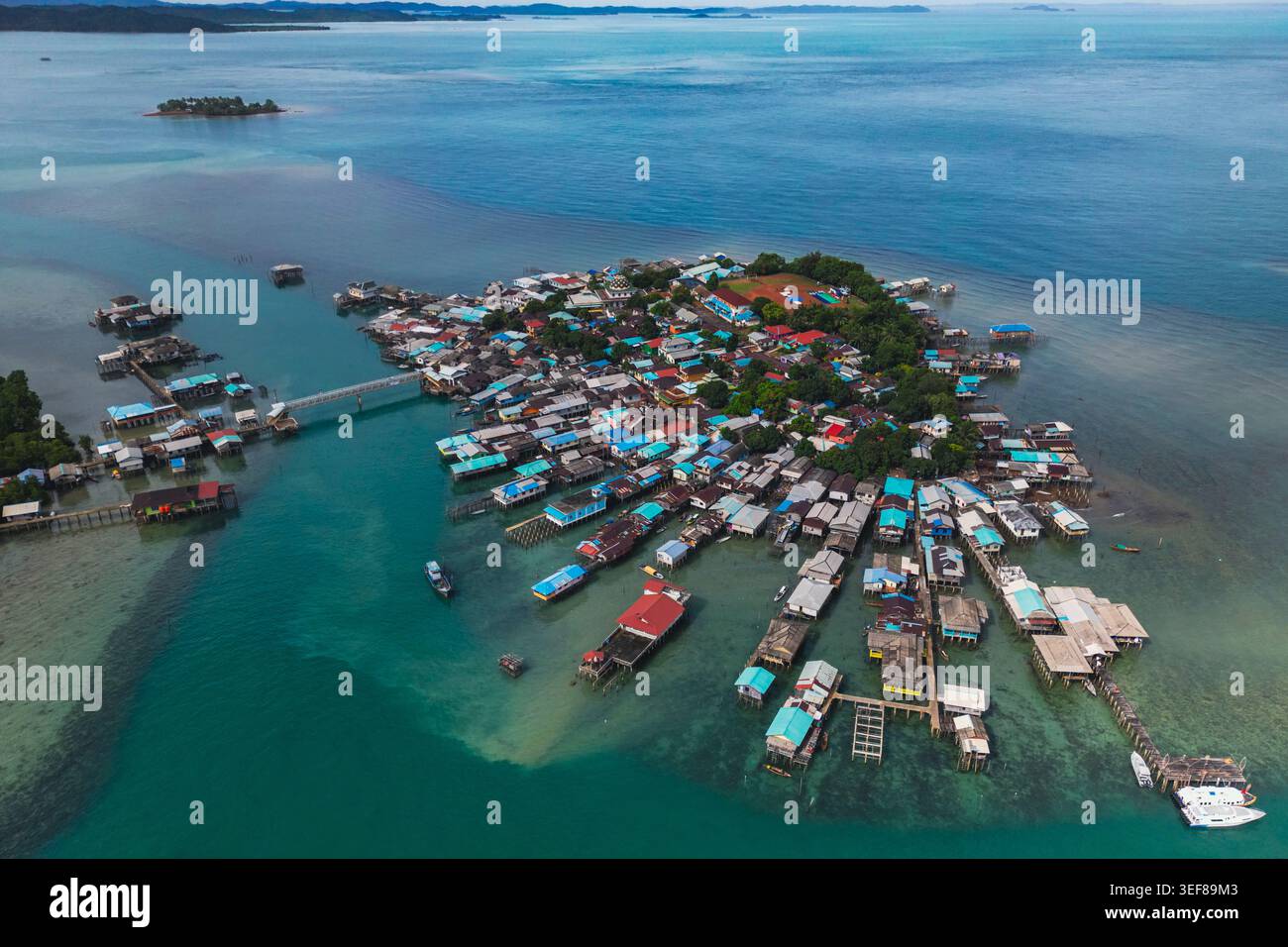Vista aerea di un tradizionale villaggio a palafitte con tetti colorati circondato da acque turchesi e lussureggiante vegetazione di Kepulauan Riau, Indonesia. Foto Stock