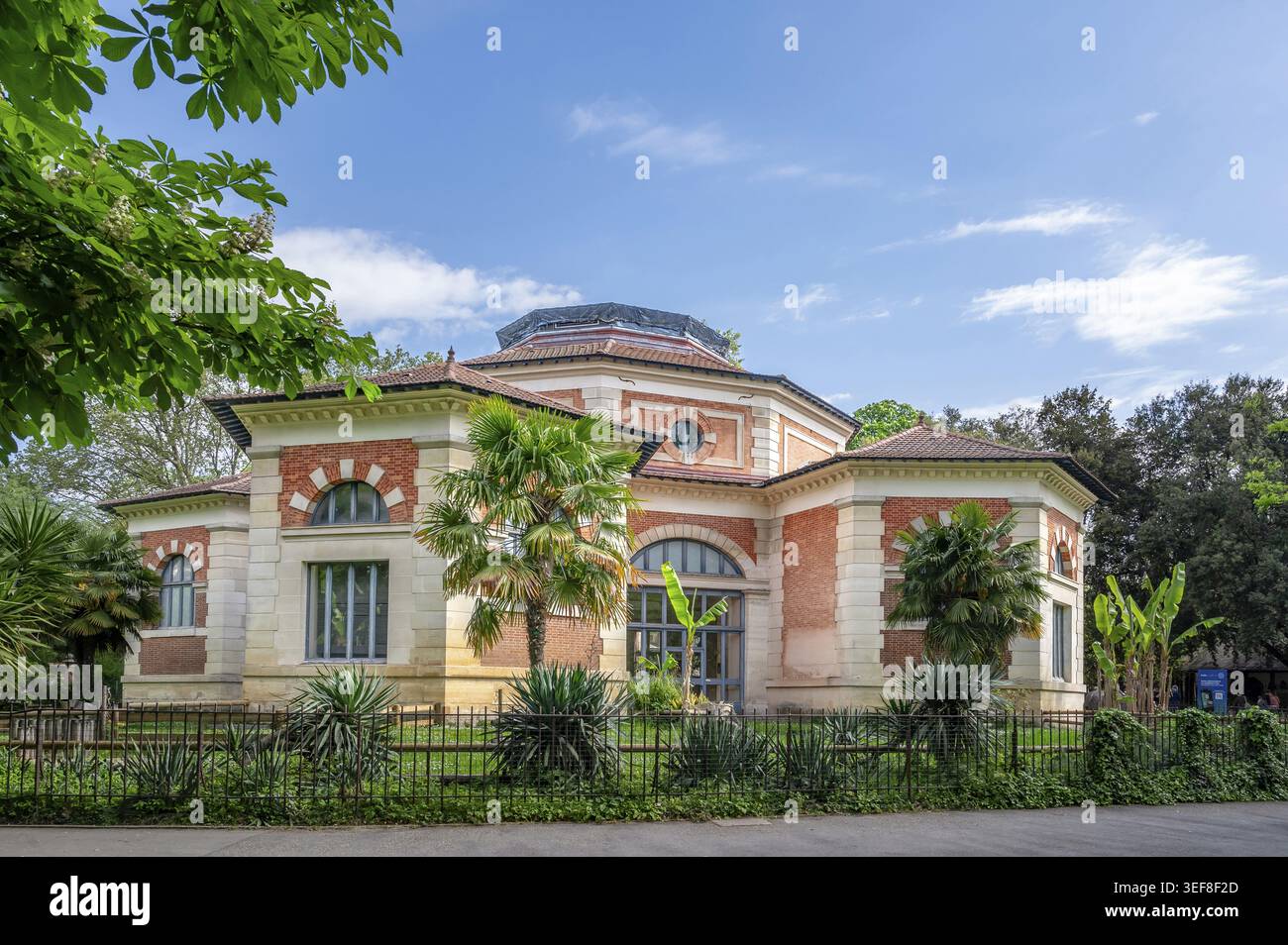 La storica casa di rettili fatta di mattoni rossi e arenaria chiara, conosciuta come il Palais des reptiles, si presenta dietro piante esotiche e palme Foto Stock