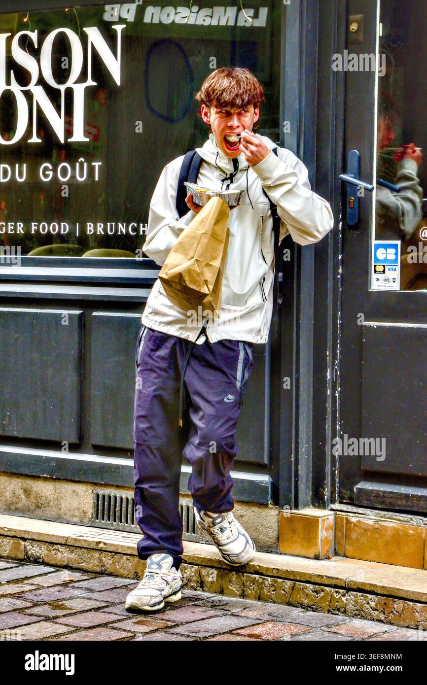 Adolescente/studente che mangia cibo da asporto mentre si trova all'ingresso del ristorante - Tours, Indre-et-Loire (37), Francia. Foto Stock
