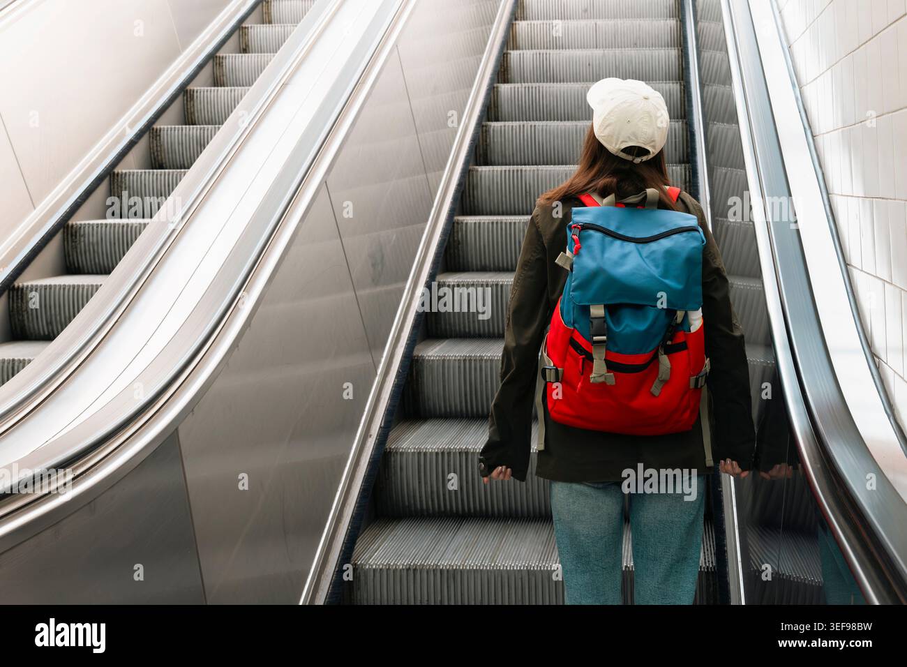 Giovane donna con uno zaino su una scala mobile in una stazione ferroviaria, che mette in risalto le moderne infrastrutture di viaggio e di transito. Foto Stock